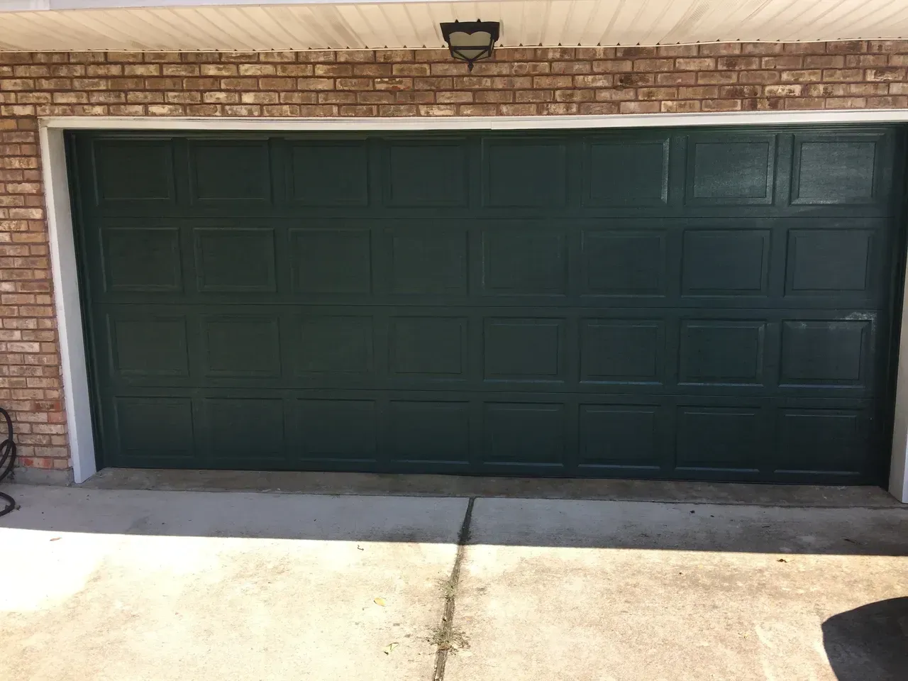 Green garage door with square panels, set in a brick and concrete setting.