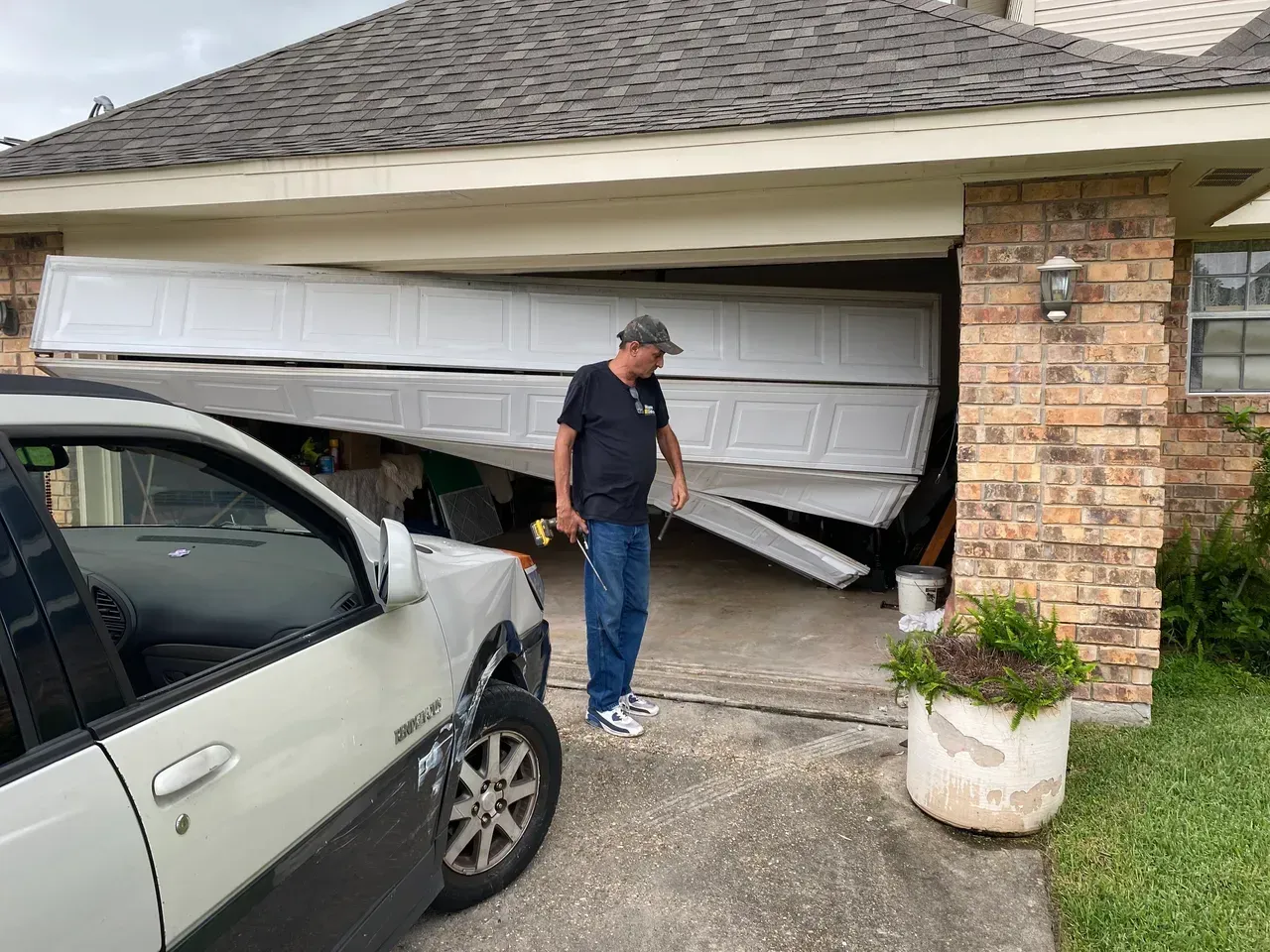 Man looking at damaged garage door; car with front damage in driveway.