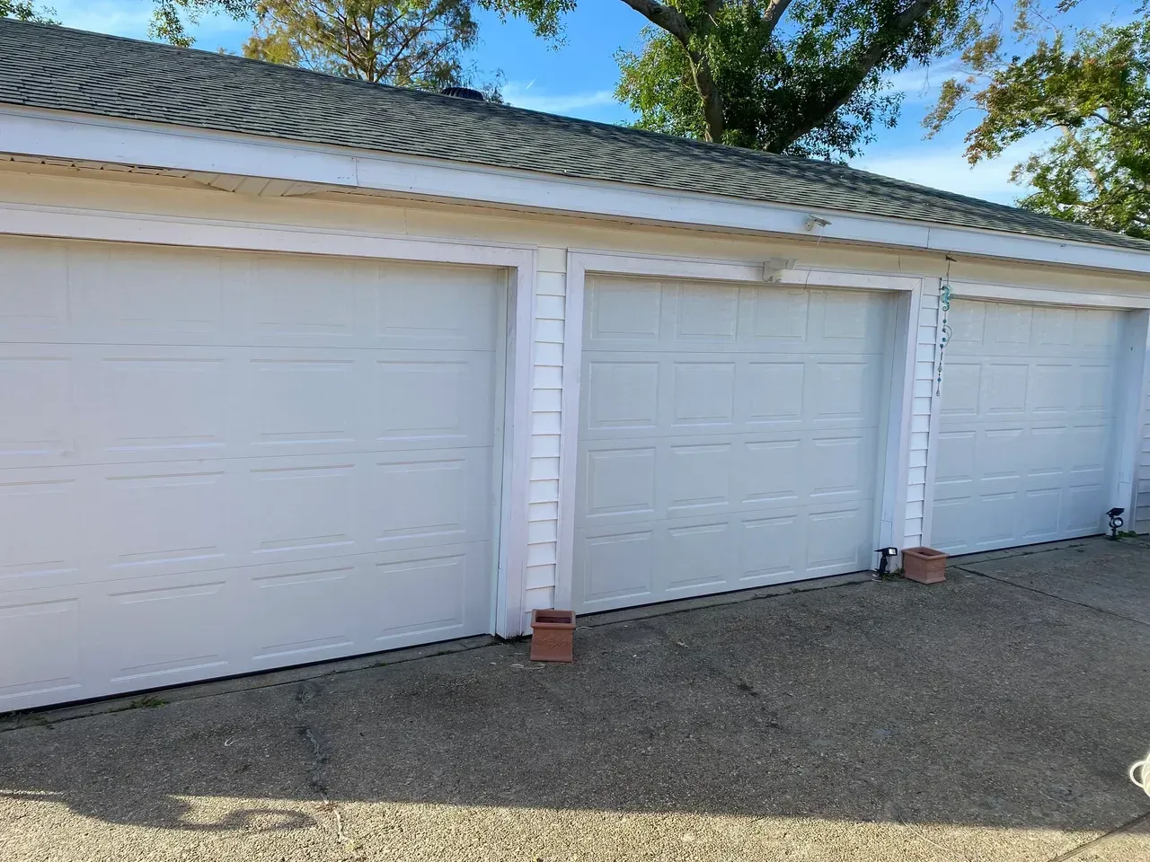 Three white garage doors with a gray roof and gravel driveway.