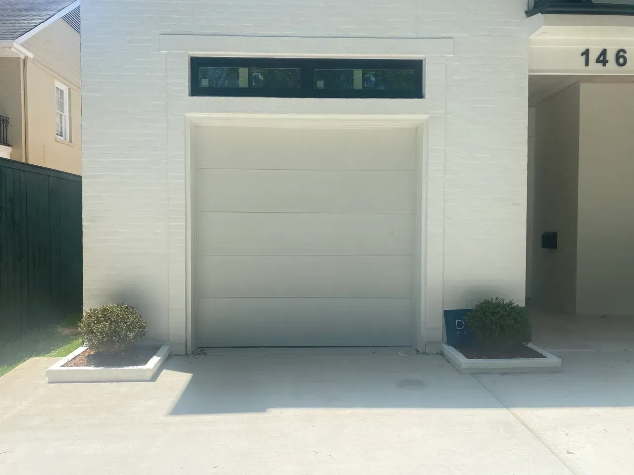 White garage door with rectangular window above, flanked by planters.