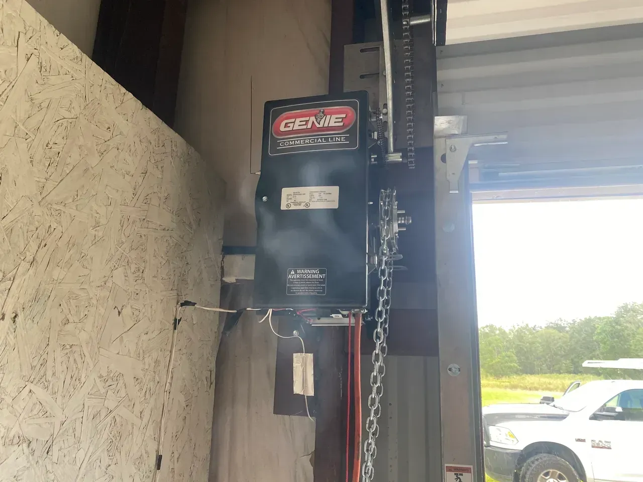 Garage door opener mounted on a wall. It has a black motor and chain with a red and white Genie logo.