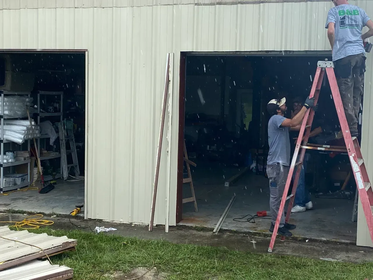 Construction workers at a garage, installing a door frame. Metal building with tools and debris.