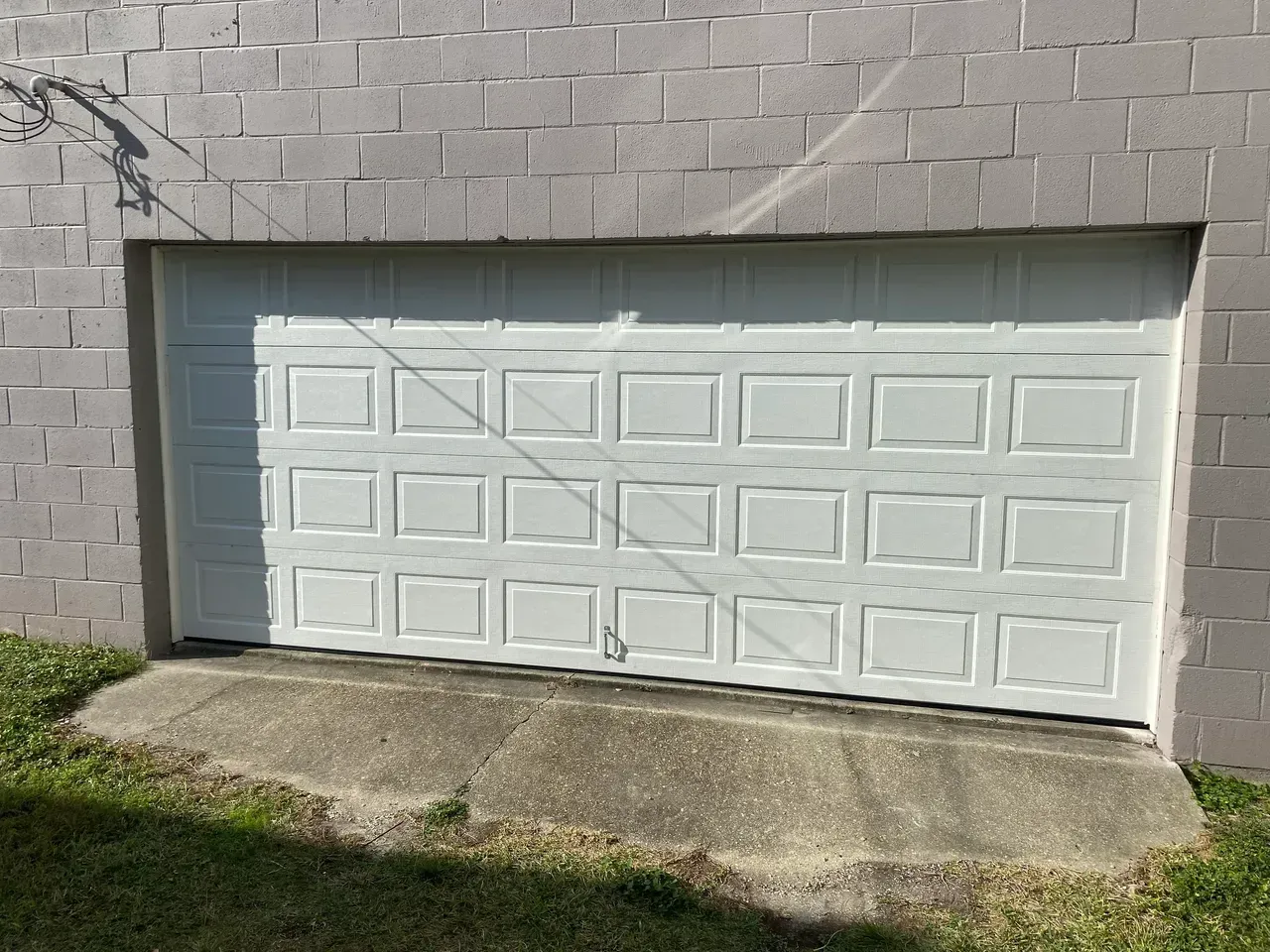White garage door set in a gray brick wall, with concrete ramp.