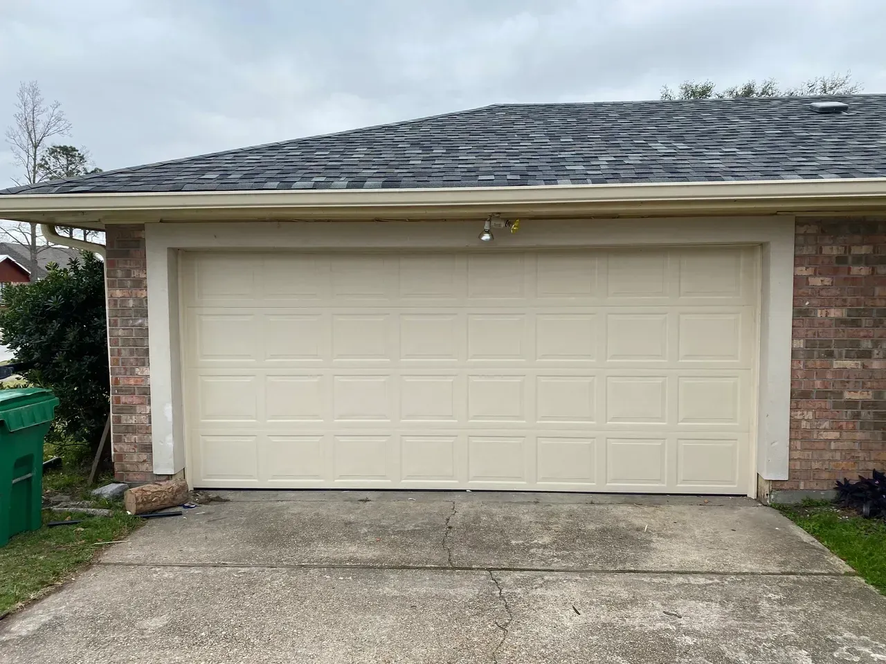 Tan garage door with brick accents and a gray roof. Concrete driveway in front.
