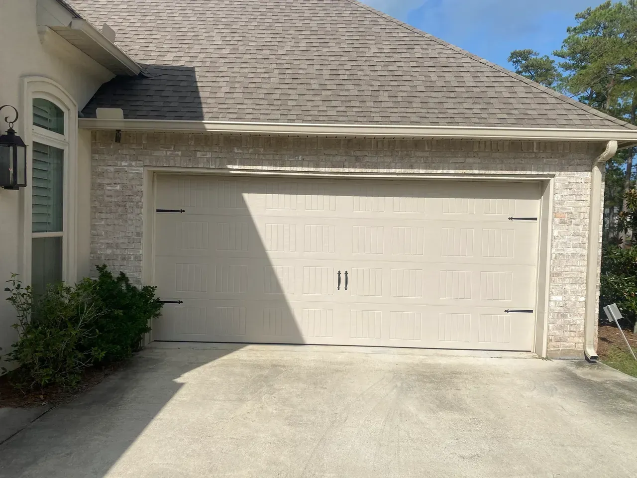 Tan garage door on a brick house with a concrete driveway.