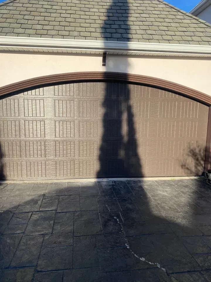 Brown garage door with arched top and shadow cast on the concrete driveway.