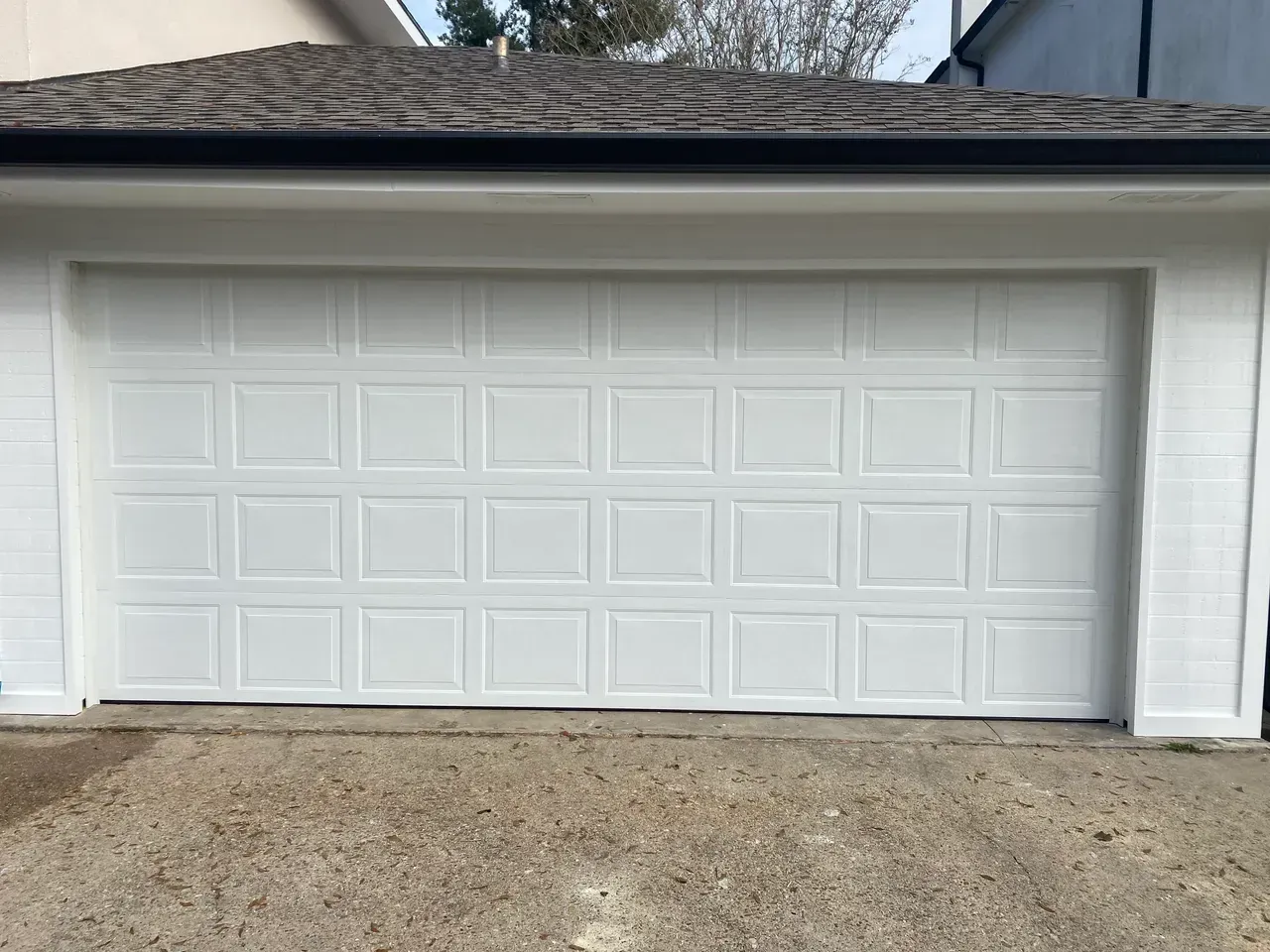 White garage door with rectangular panels, set in a light-colored, gravel-covered area.