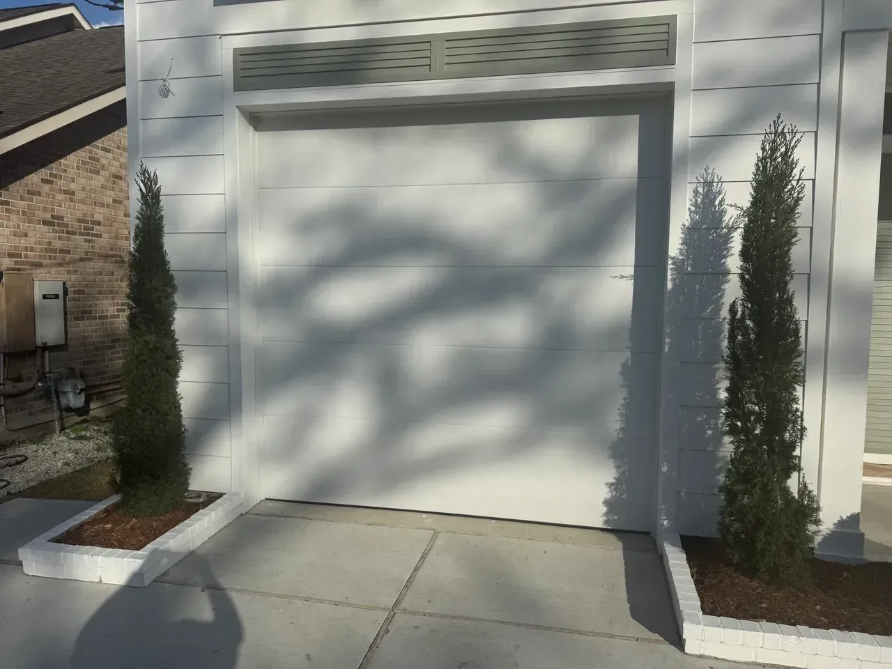 White garage door with two potted, tall, thin trees.