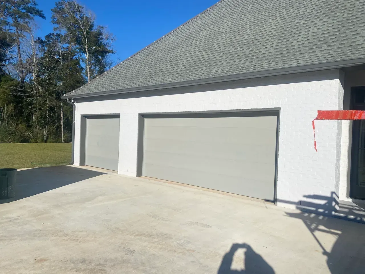 Two-car garage with gray doors on a white stucco building, concrete driveway, blue sky.