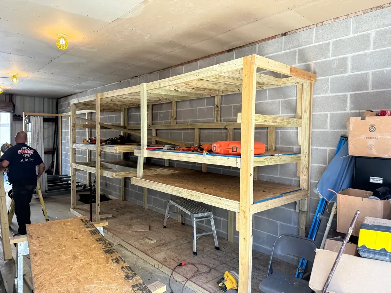 Wooden shelving unit against a cinder block wall, with tools and objects on the shelves. A person walks by.