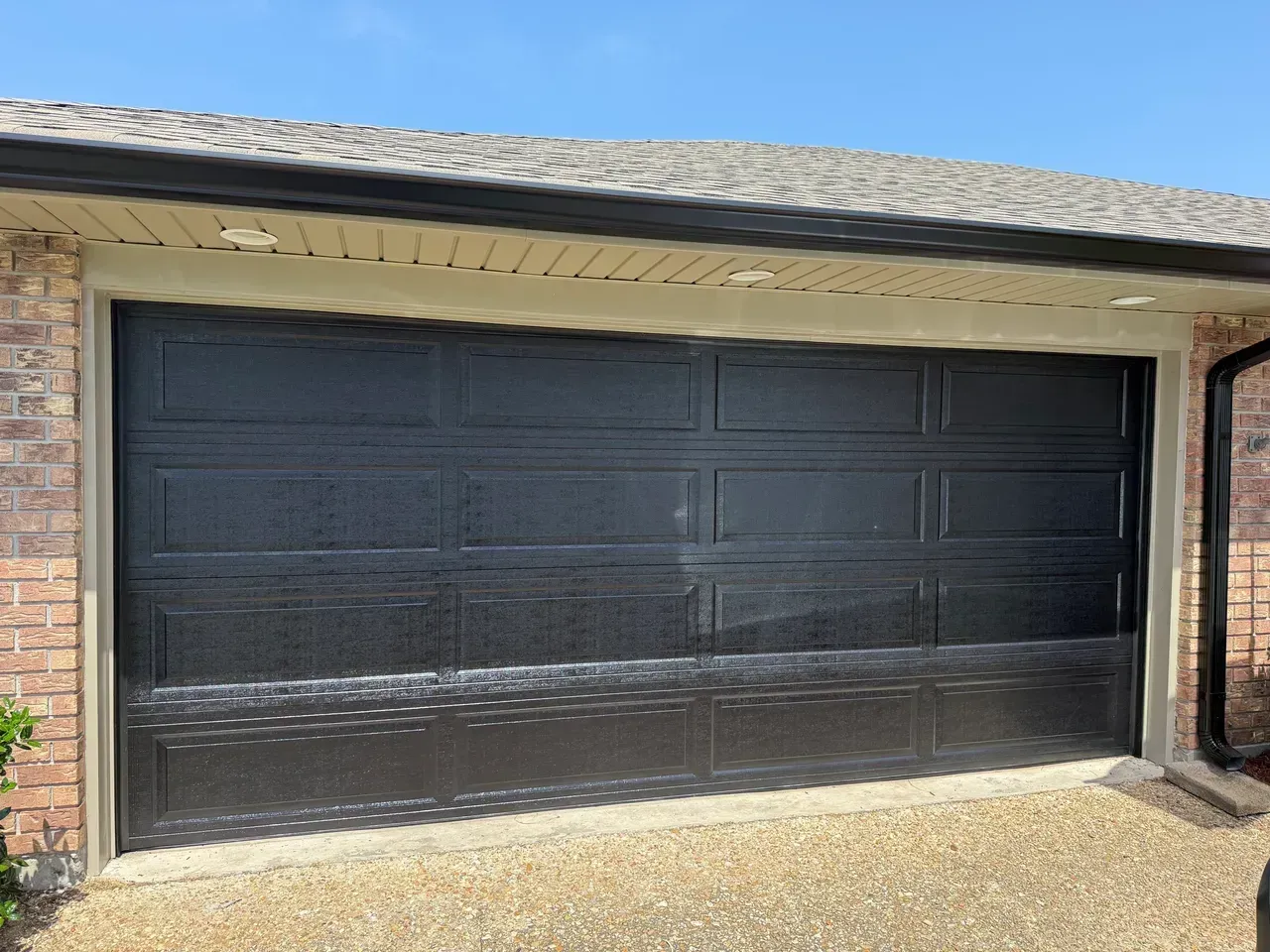 Black garage door on a brick building with a gravel driveway.