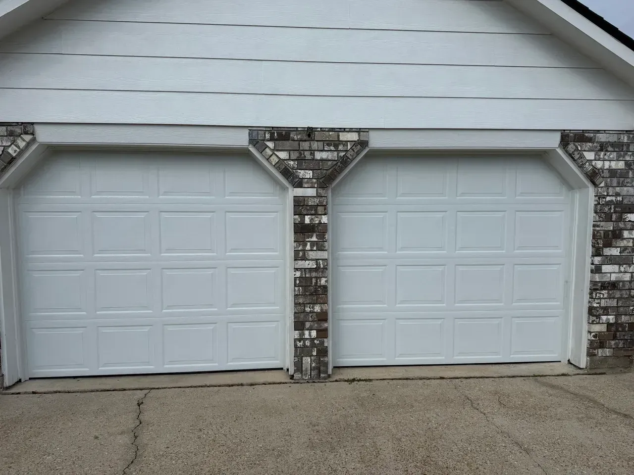Two white garage doors with brick accents.