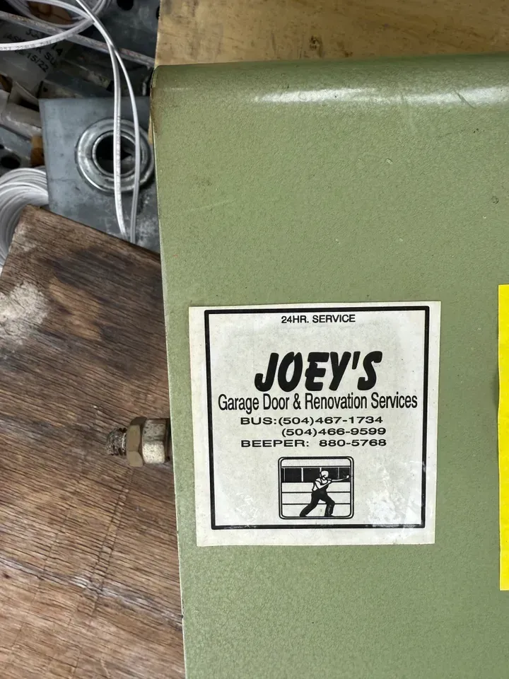 A green metal box with a white label: Joey's Garage Door & Renovation Services. Contact info and a graphic of a person.