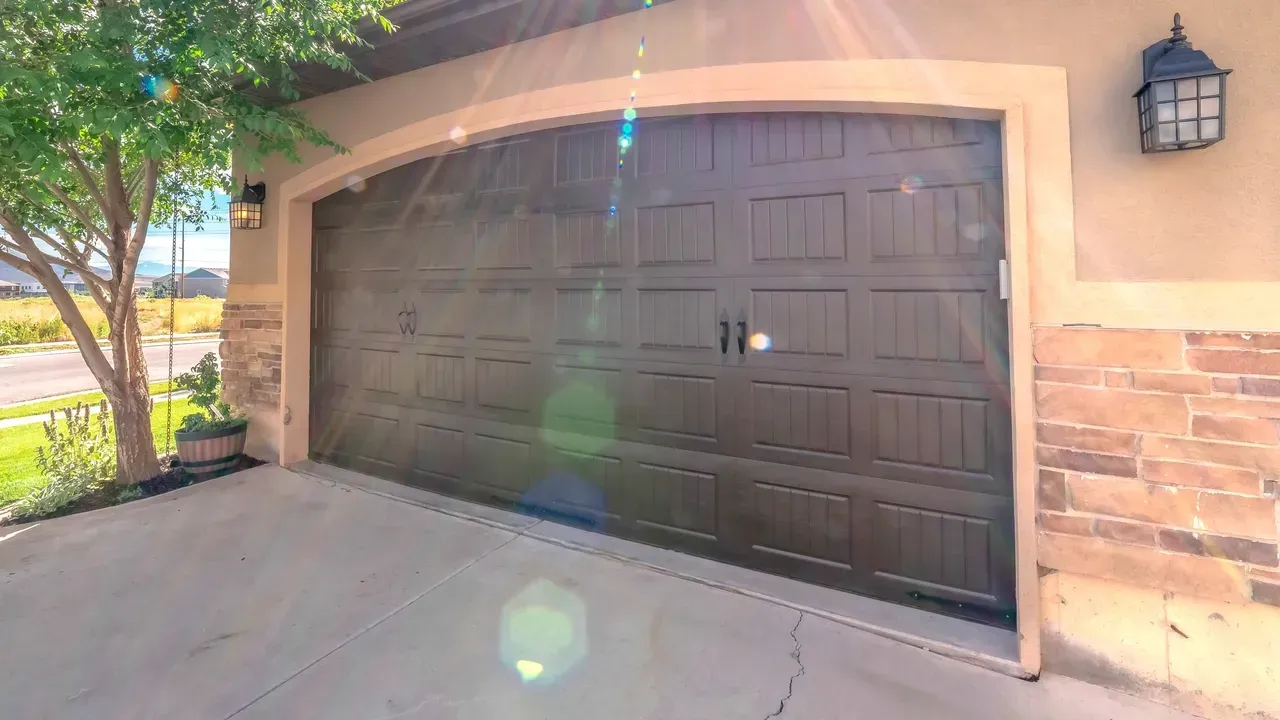 Brown garage door under an arched doorway, with a tree to the left and stone wall to the right.