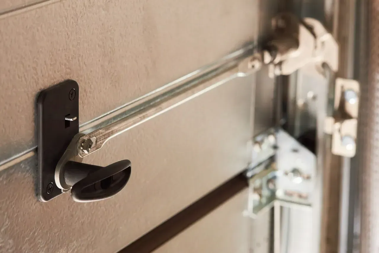 Garage door manual release lever. Black lever on a metal door with a metal arm.