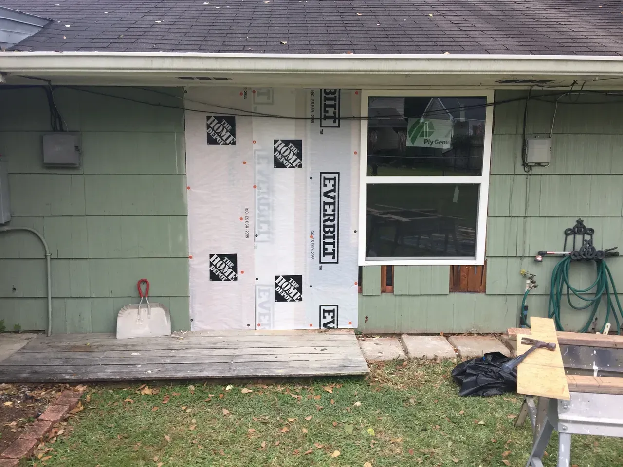 House exterior under construction, with missing siding, new sheathing, window, and porch. Green siding and gray roof.