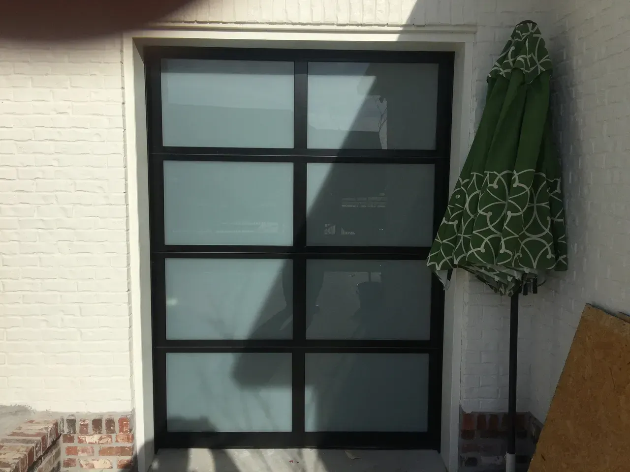 Black framed, glass panel garage door, next to a green and white patio umbrella.