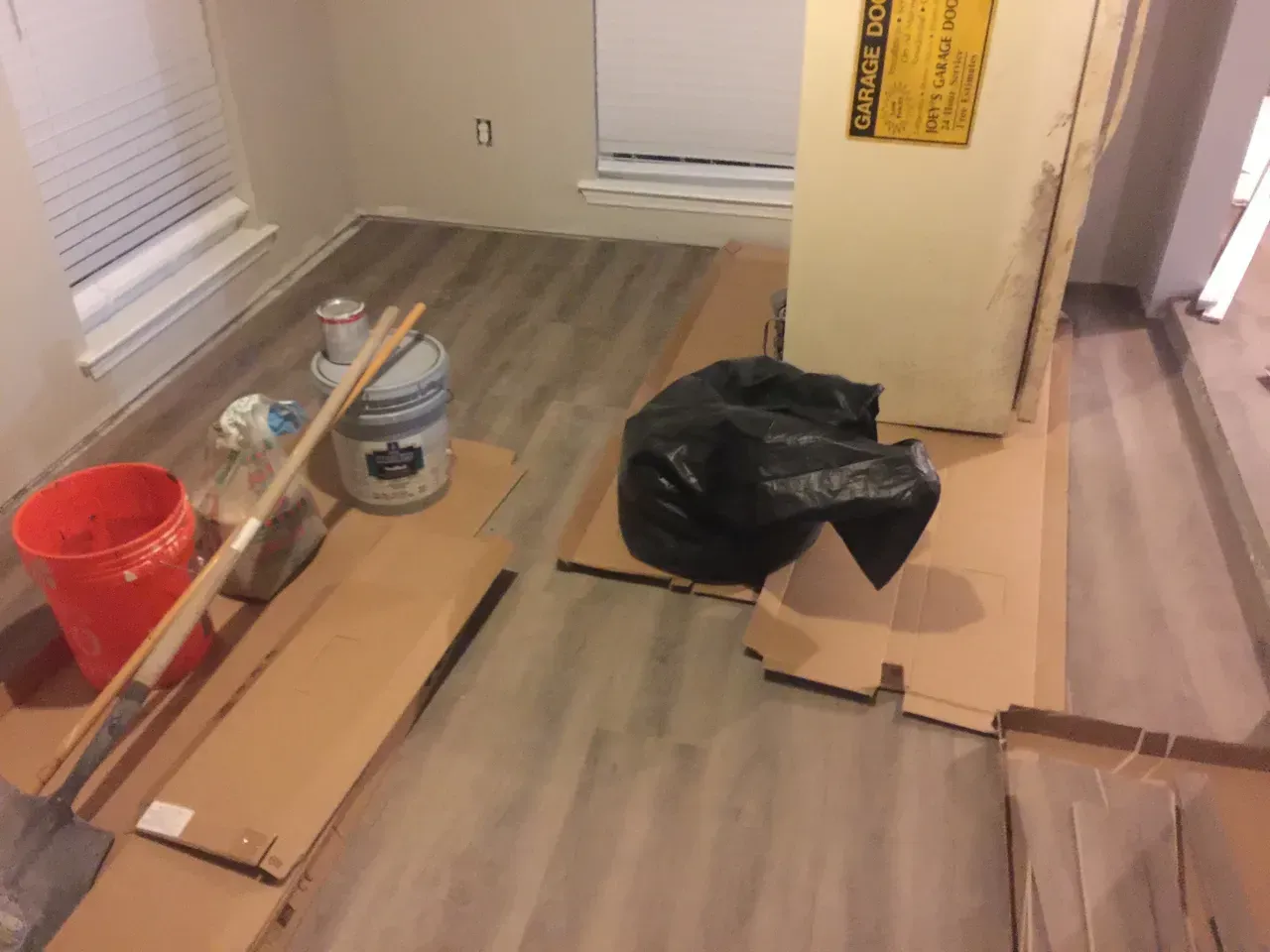 Room with new flooring, cardboard, paint supplies, and a refrigerator.