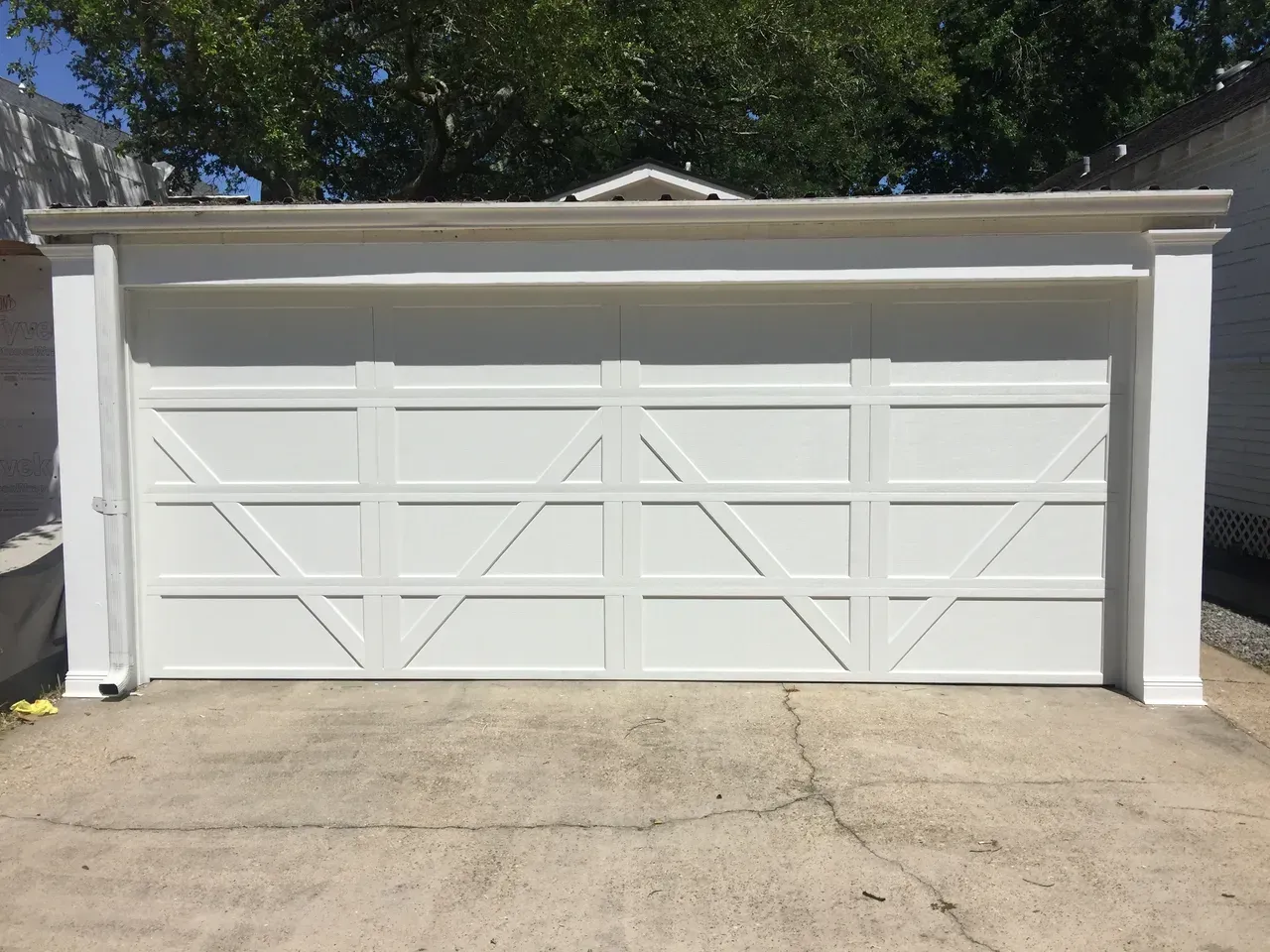White garage door with an X-pattern design. Concrete driveway, with trees in the background.