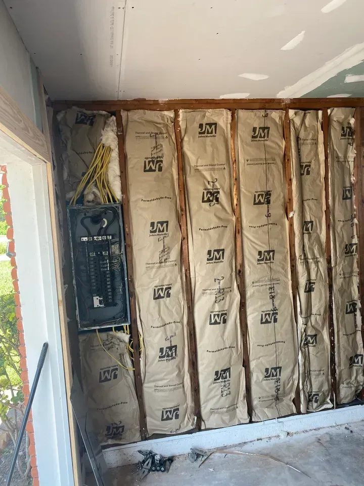 Interior wall framing with insulation, electrical panel, and unfinished drywall.