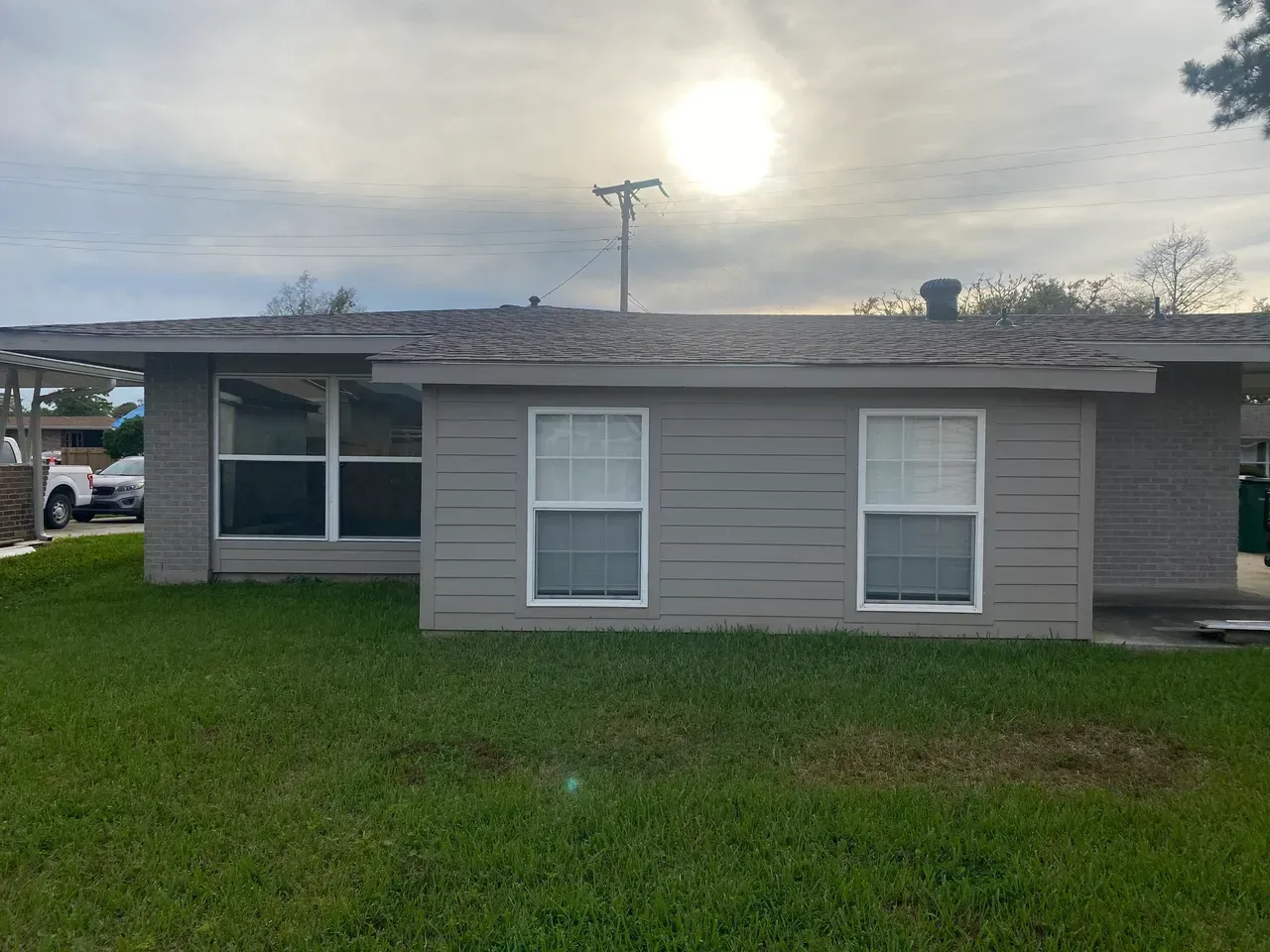 Gray house with two windows and a large picture window, under a cloudy sky.