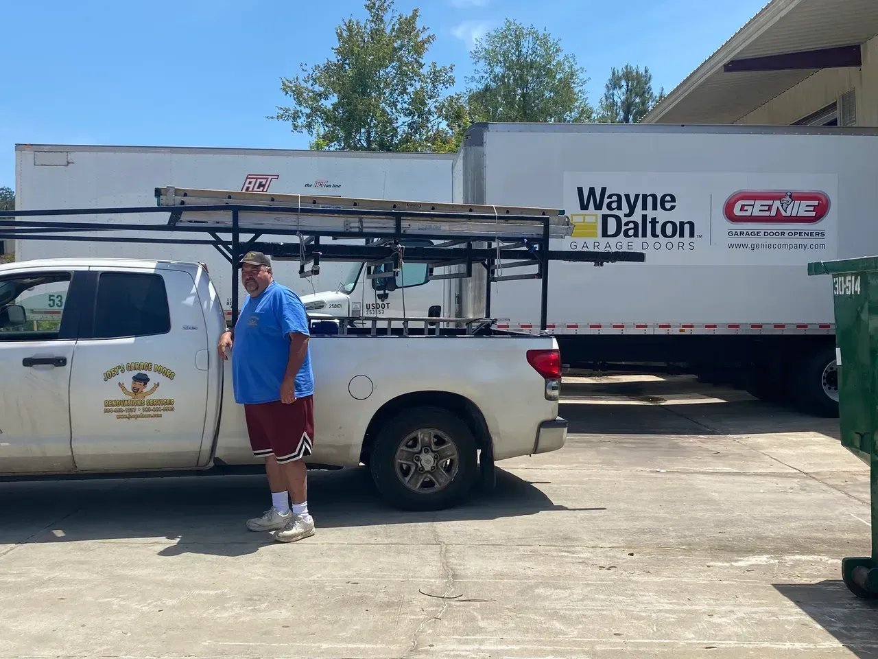 Man stands beside white work truck and a large trailer with Wayne Dalton and Genie logos.