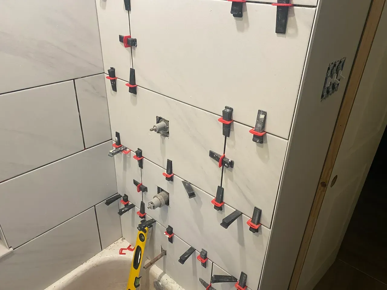 White tiled bathroom wall under construction with leveling clips.