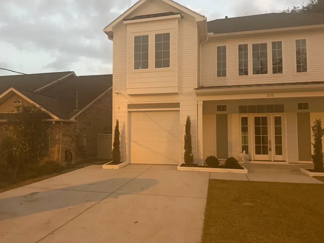 Two-story white house with a garage and double doors. Gray driveway, green grass, and small trees.