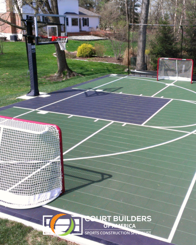 A backyard multi-sport game court featuring green and dark blue tiles, a basketball hoop, and two hockey nets on a lawn.