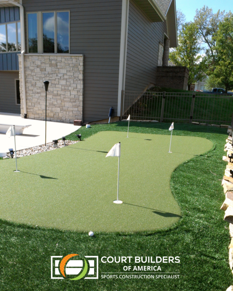 Backyard putting green with multiple holes and white flags, located next to a house patio.