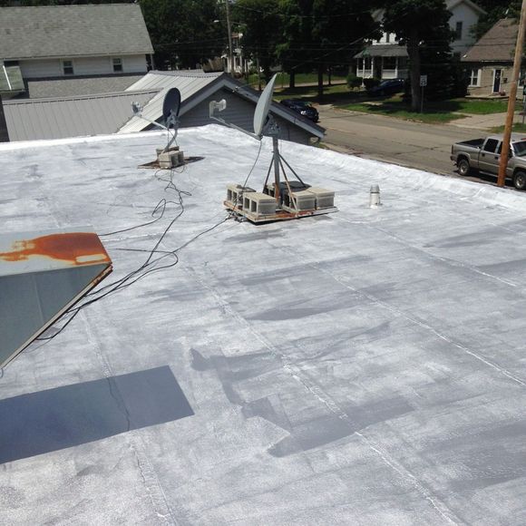 Flat white roof with satellite dishes and cables, viewed from above in a residential neighborhood