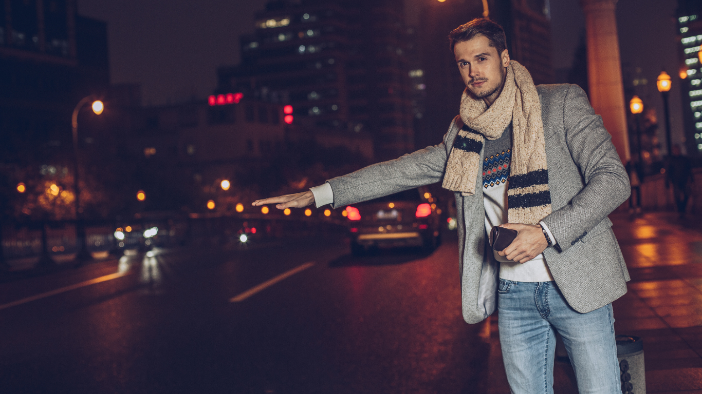 A man is hailing a taxi on a city street at night.