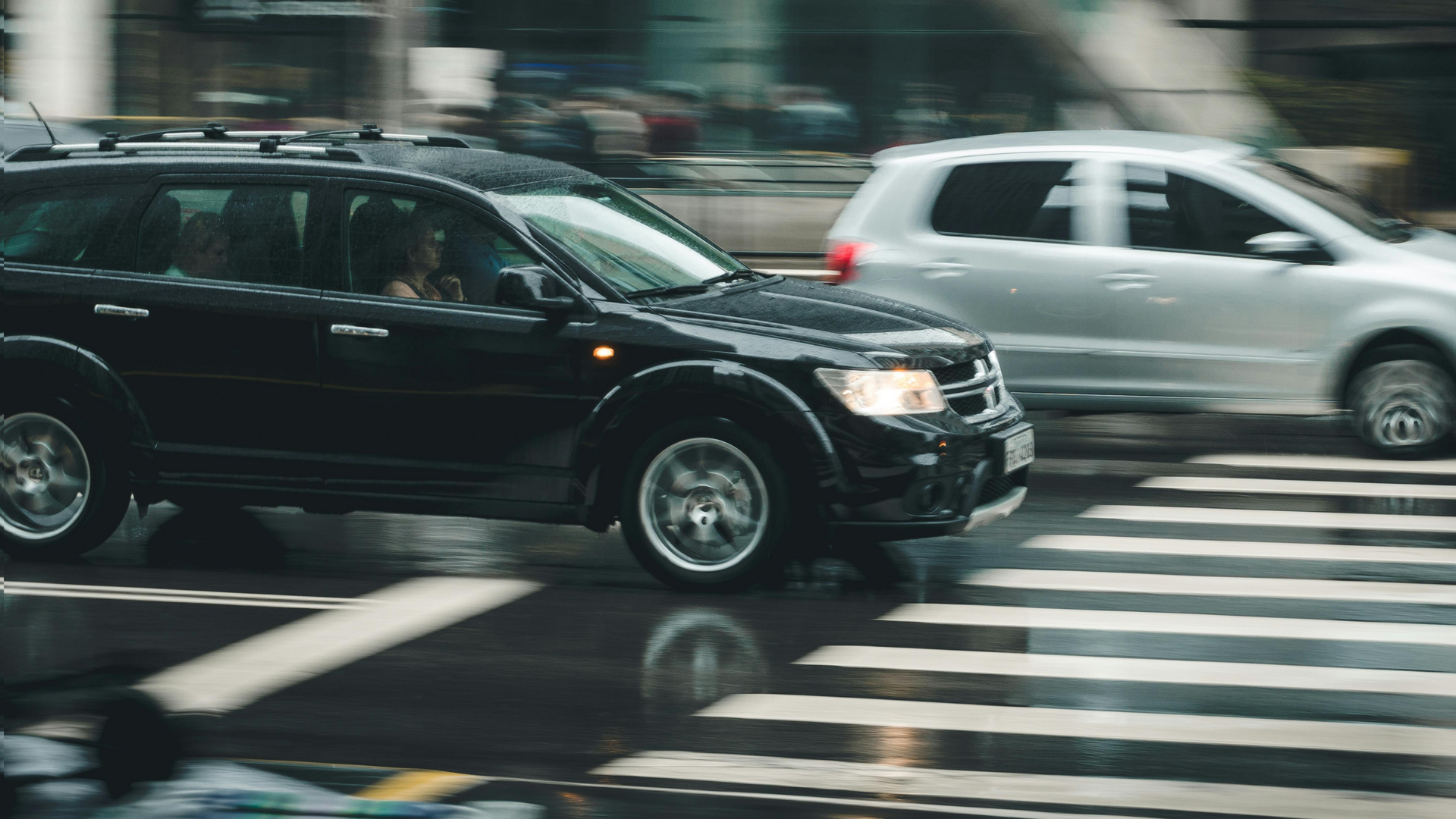 A black suv and a white van are driving down a wet street.