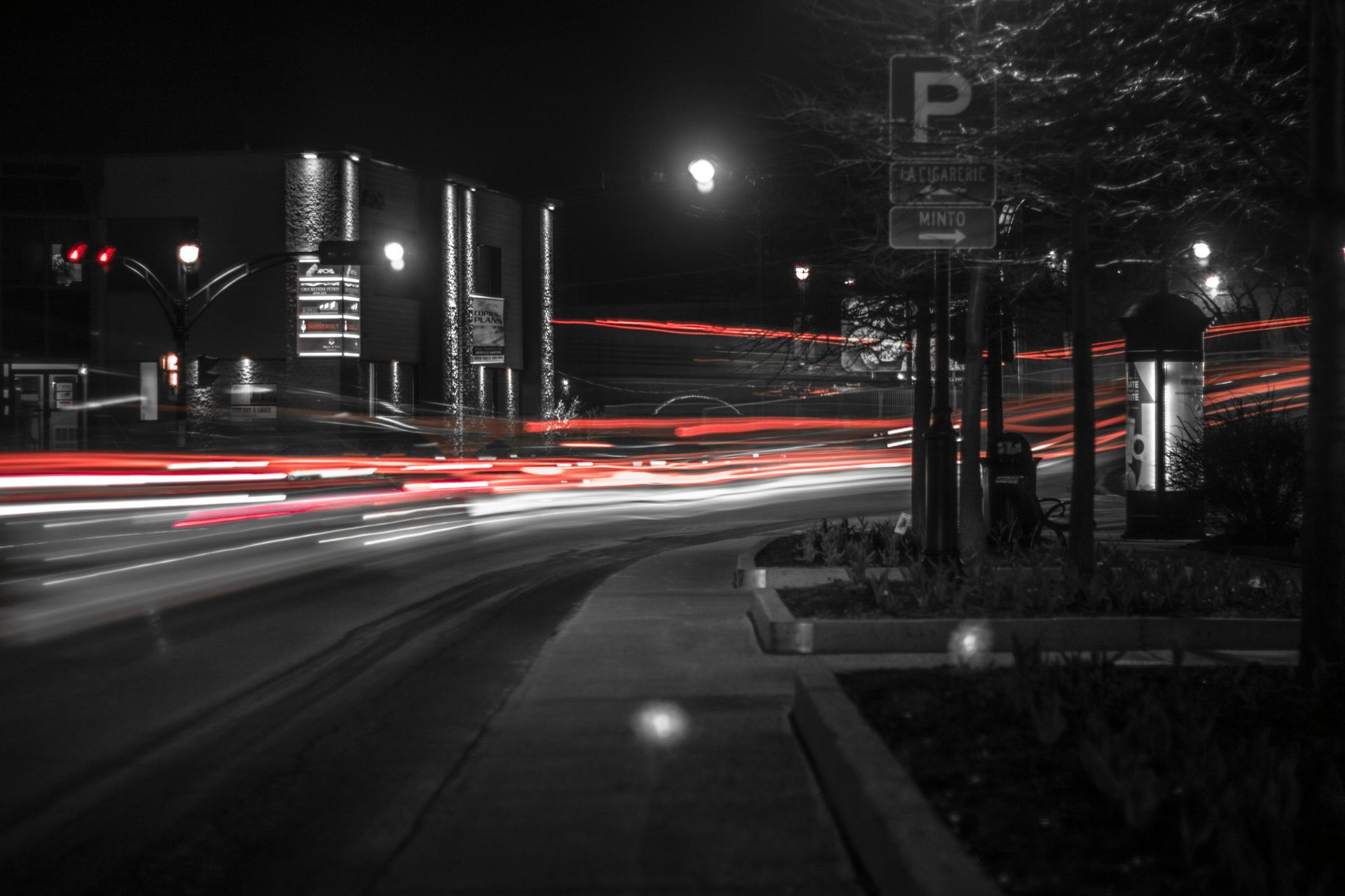 A black and white photo of a street at night with a parking sign in the foreground.