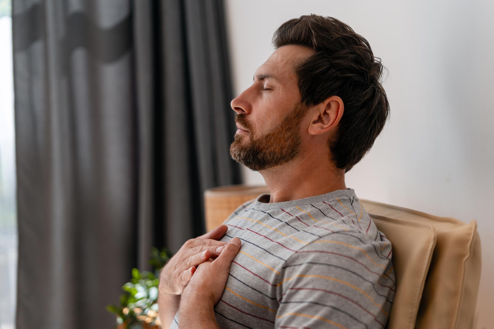 Man leaning back in a chair, eyes closed, hands on chest, in a calm indoor setting