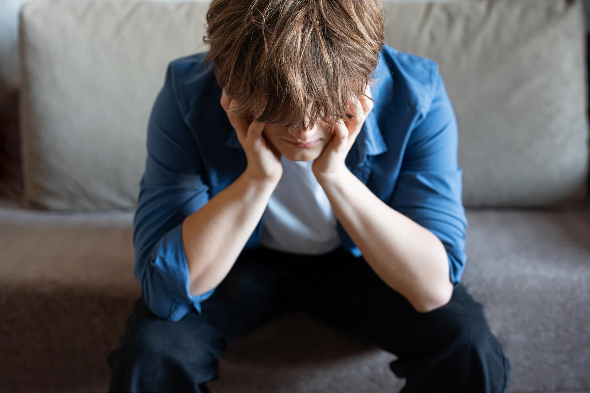 Person sitting on a couch, head in hands, looking distressed