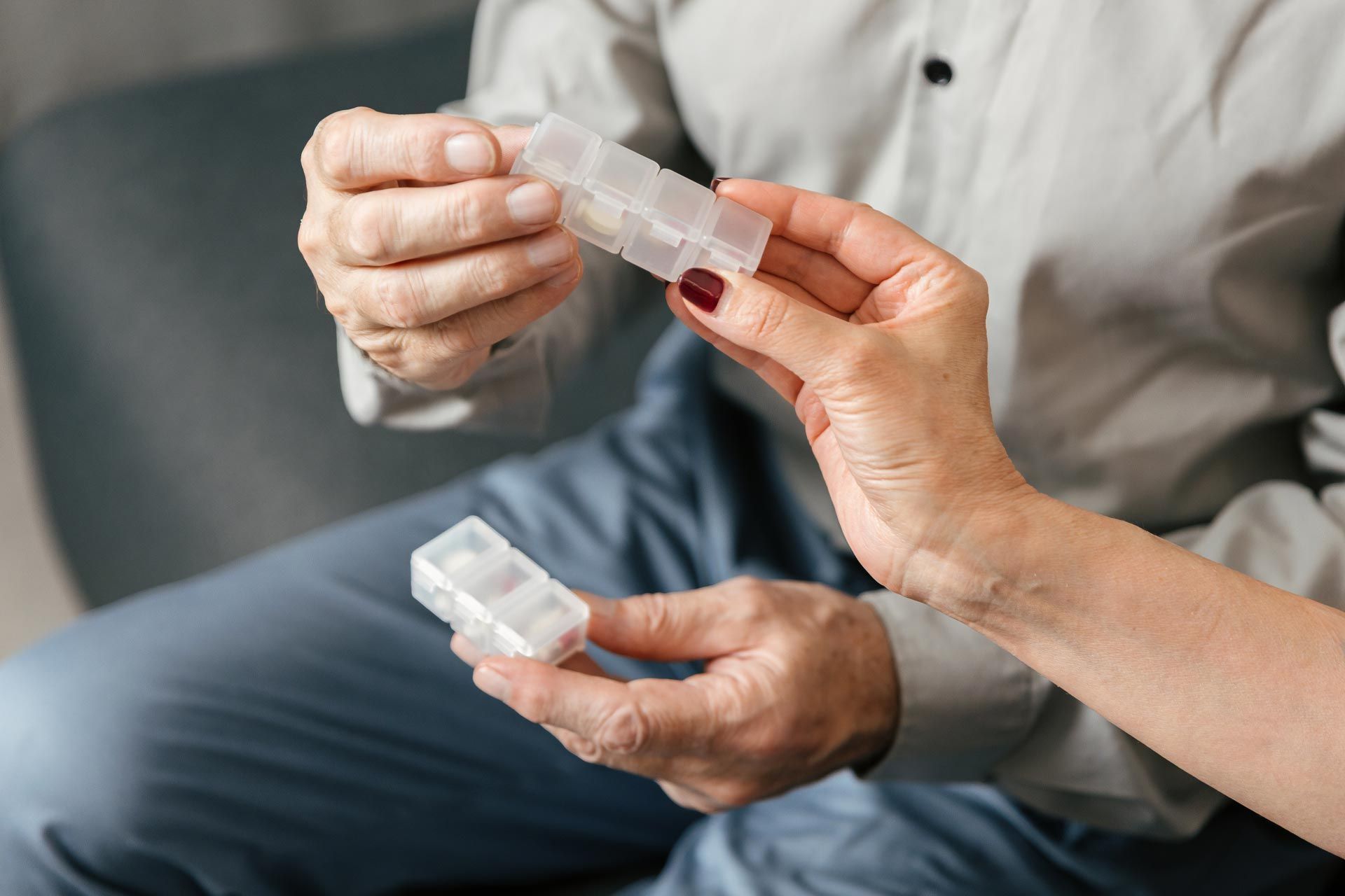Two hands holding a clear medicine pill organizer and blister packs on a couch