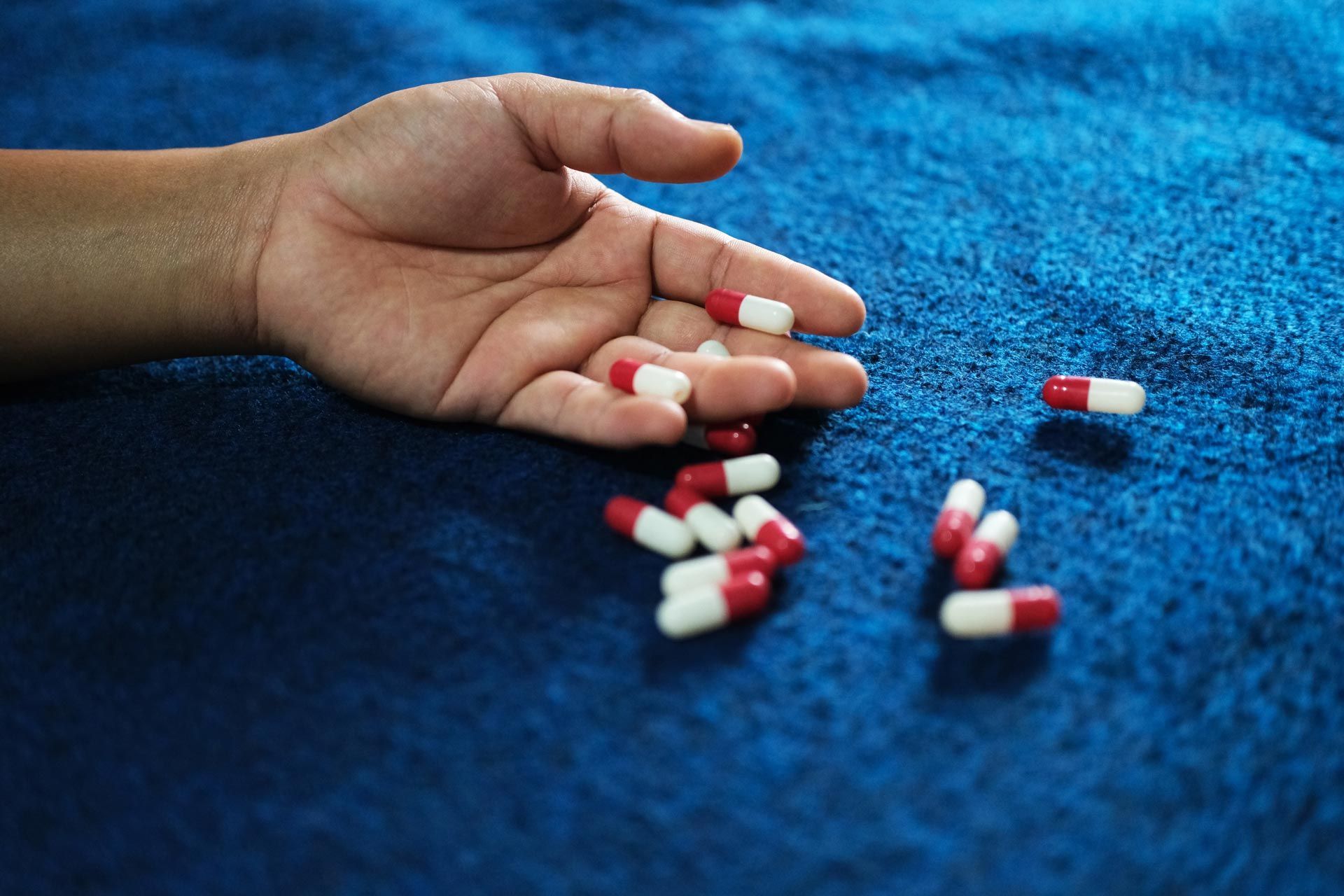 Hand holding red, white, and blue capsules spilled on a blue carpet