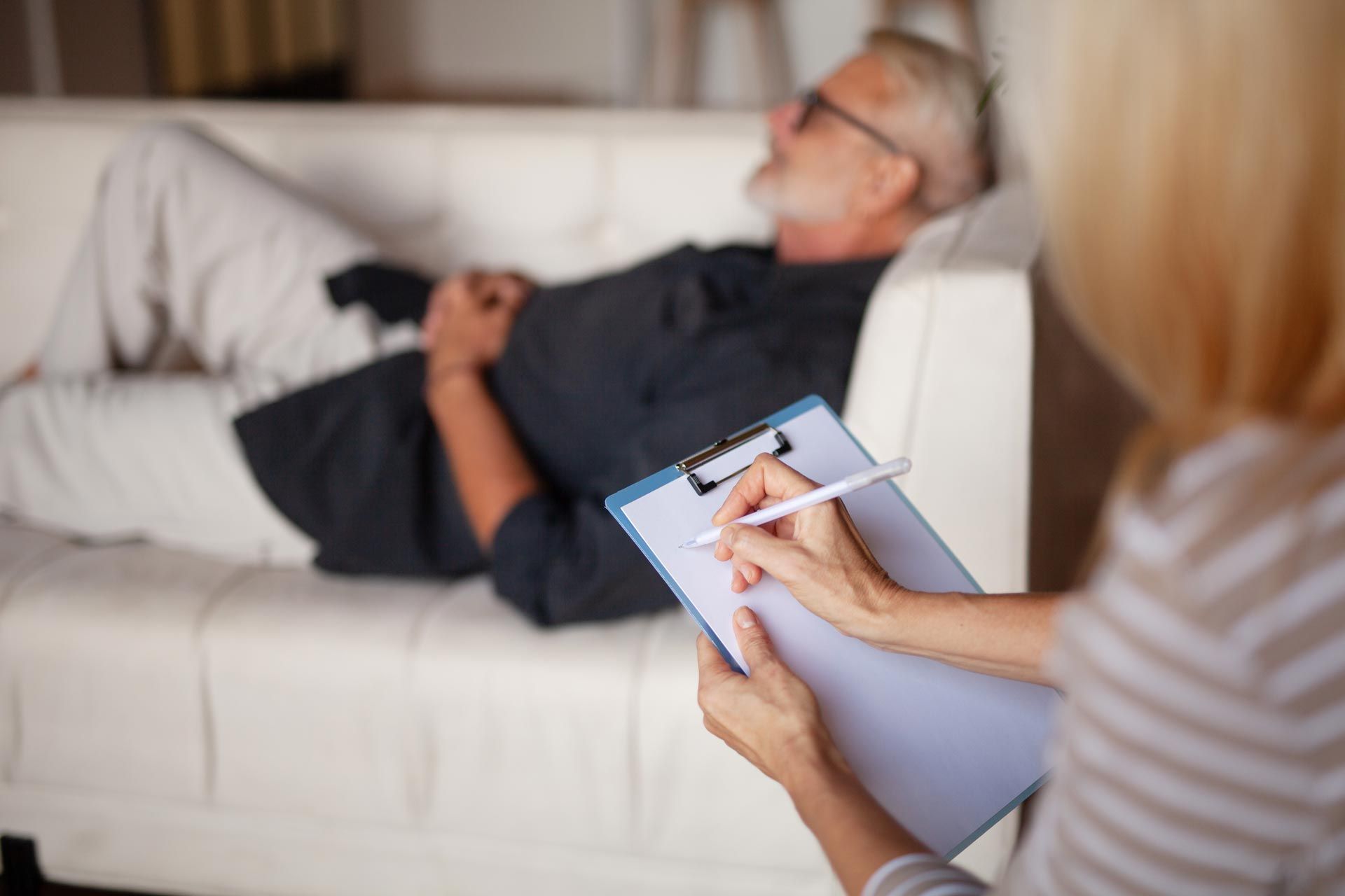 Therapist taking notes while a patient reclines on a white couch in a 상담 setting