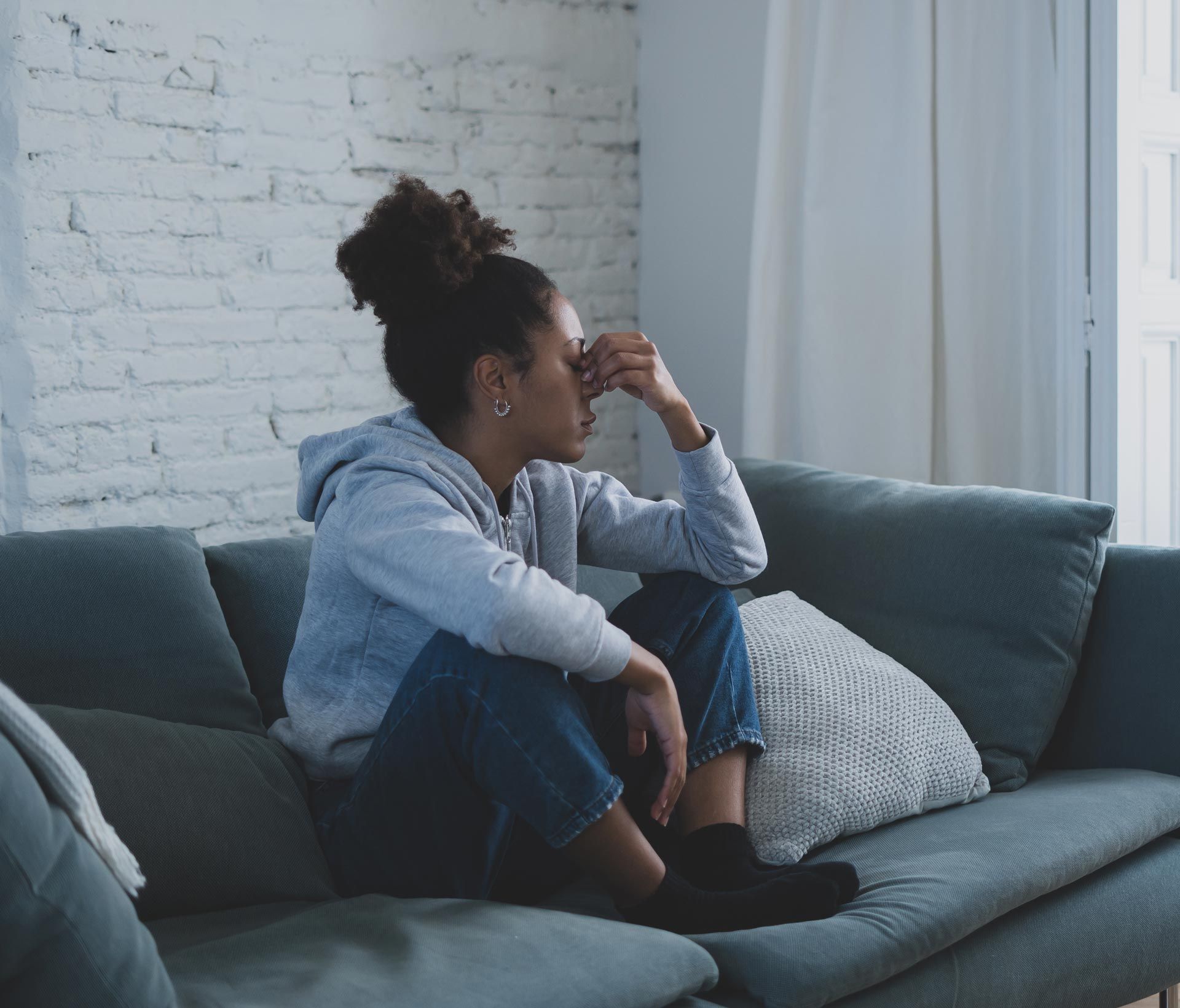 Person sitting on a couch by a window, looking out thoughtfully in a gray living room.