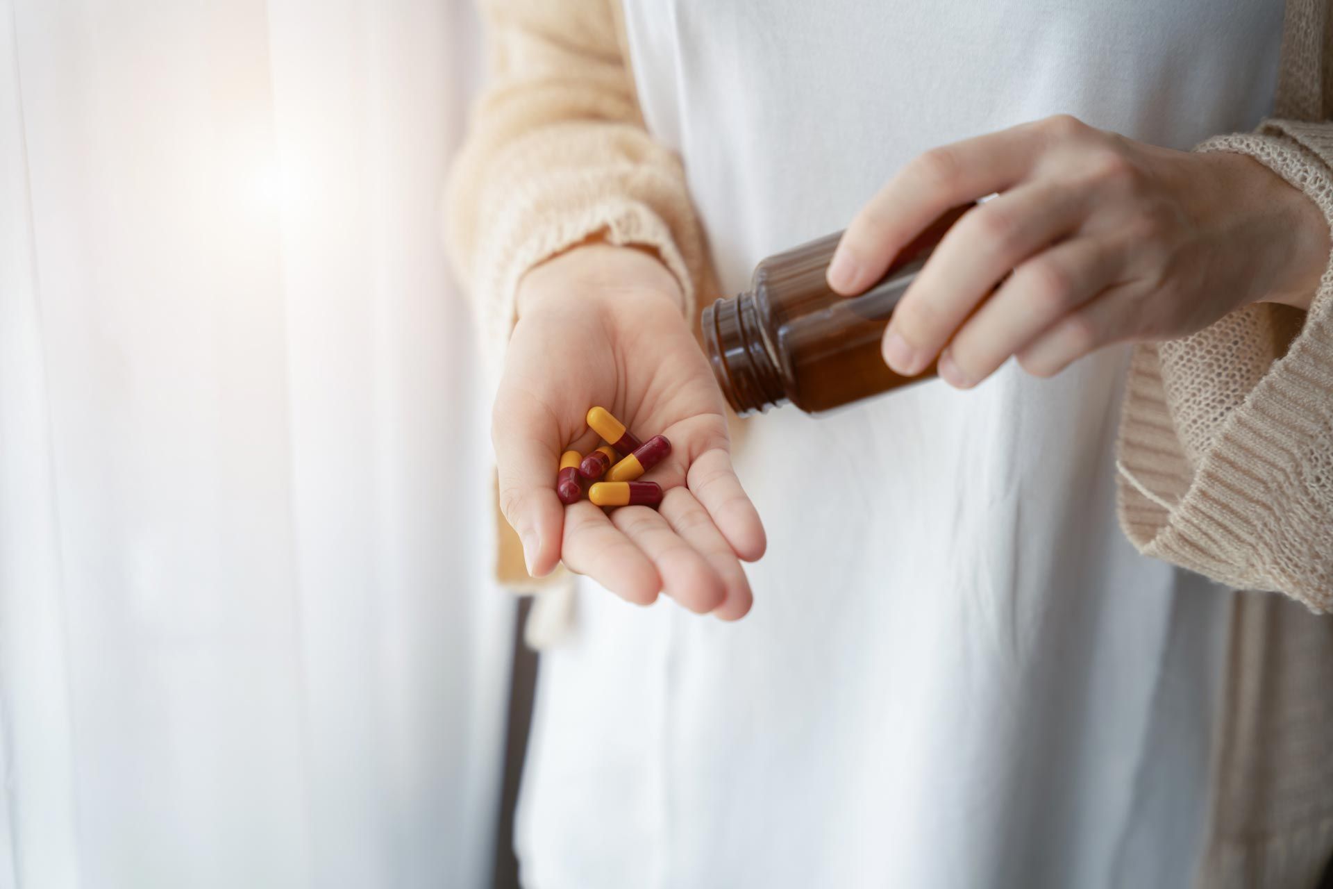 Hand pouring capsules from a brown bottle into an open palm against a white shirt
