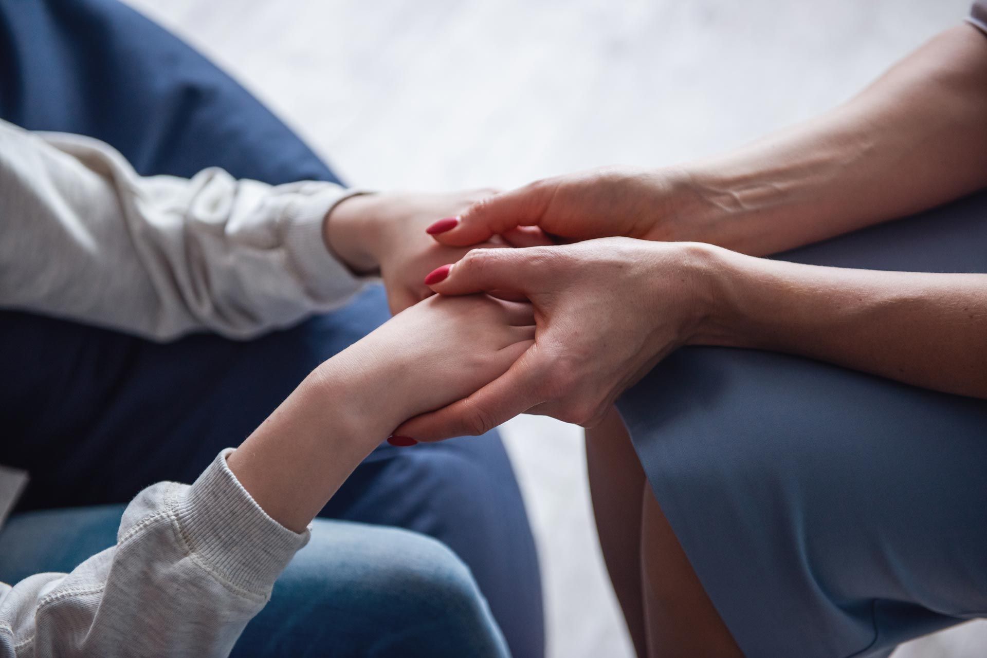 Two people holding hands in a comforting gesture on a couch