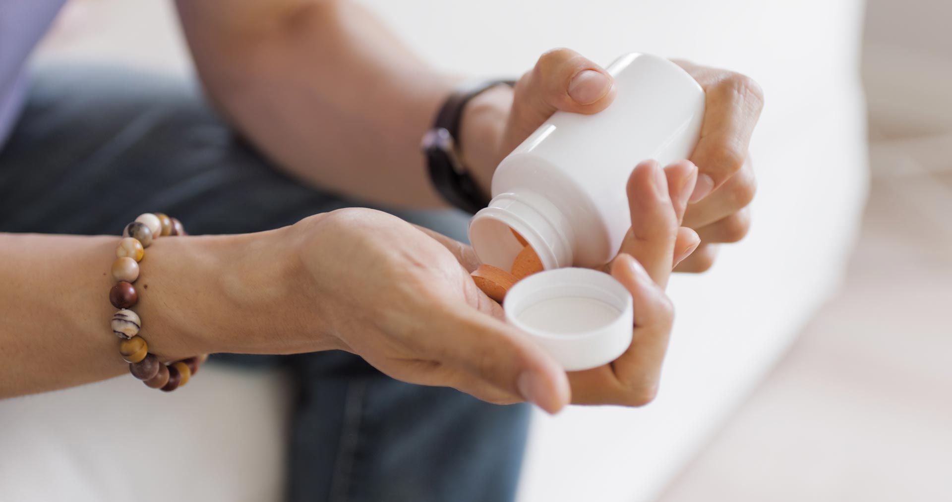 Hands holding a white pill bottle and cap, pouring medicine into the lid.