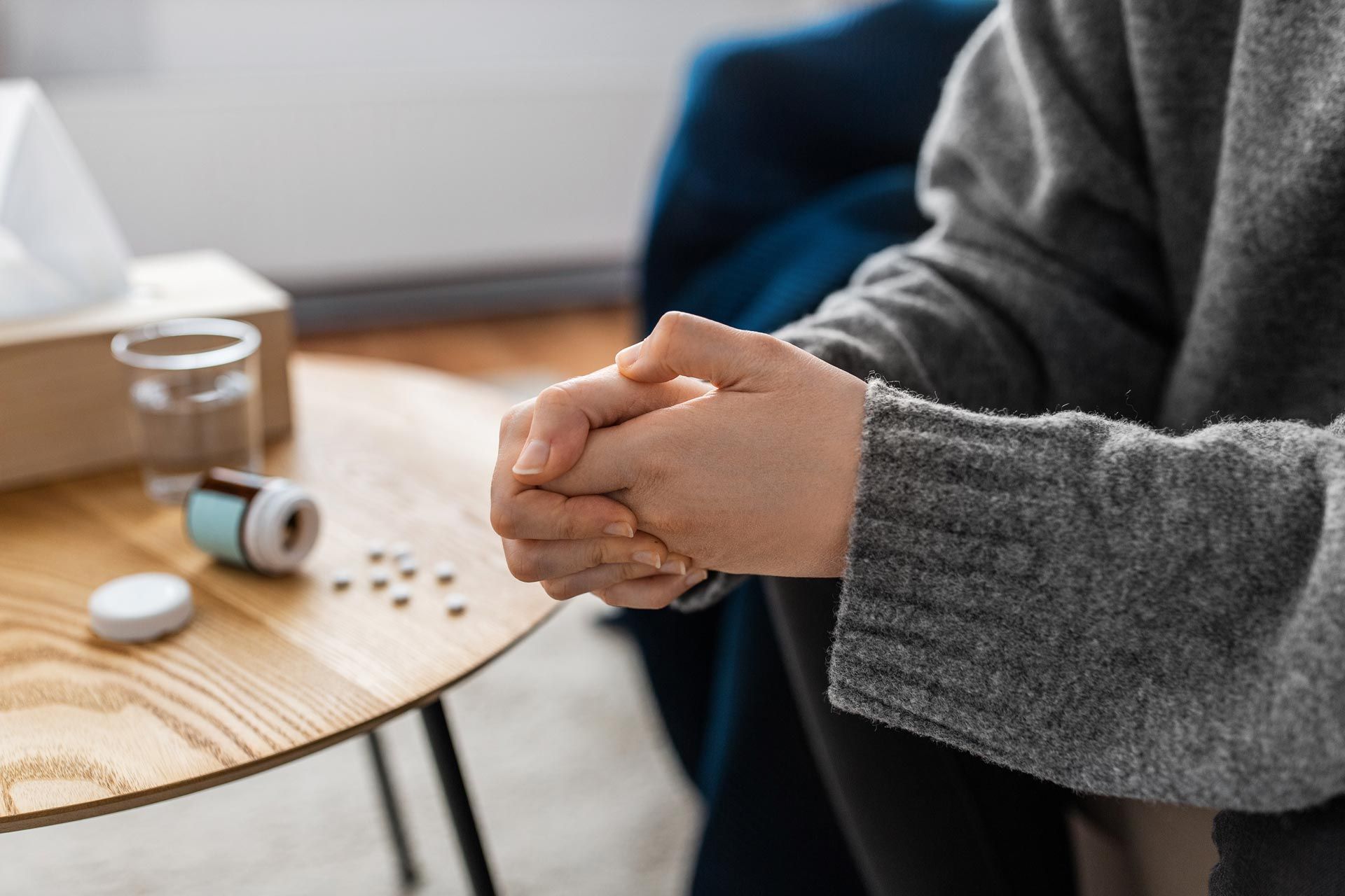 Hands clasped at a table beside medicine and a glass of water