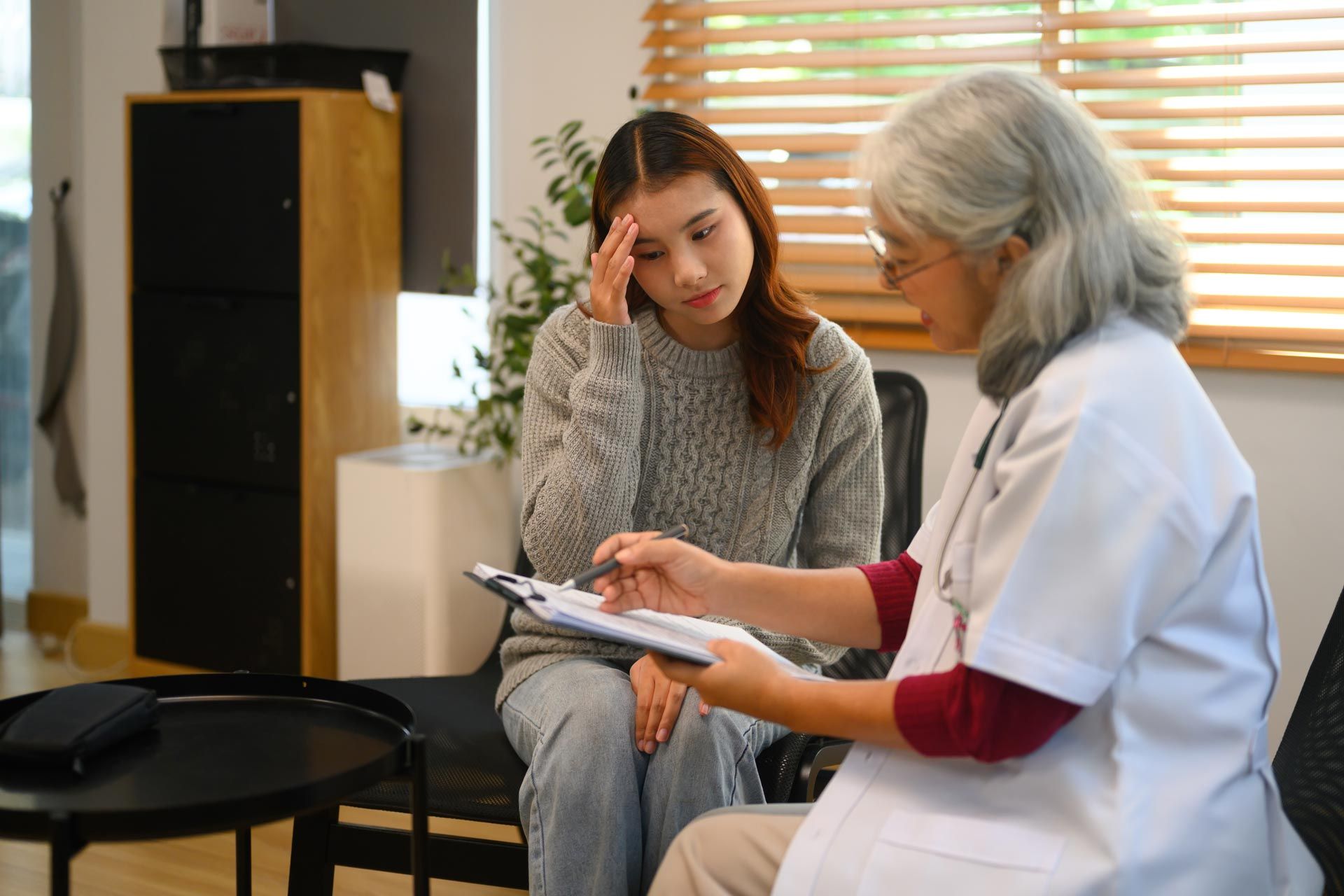 Two women in a clinic, one taking notes while the other points at a clipboard.