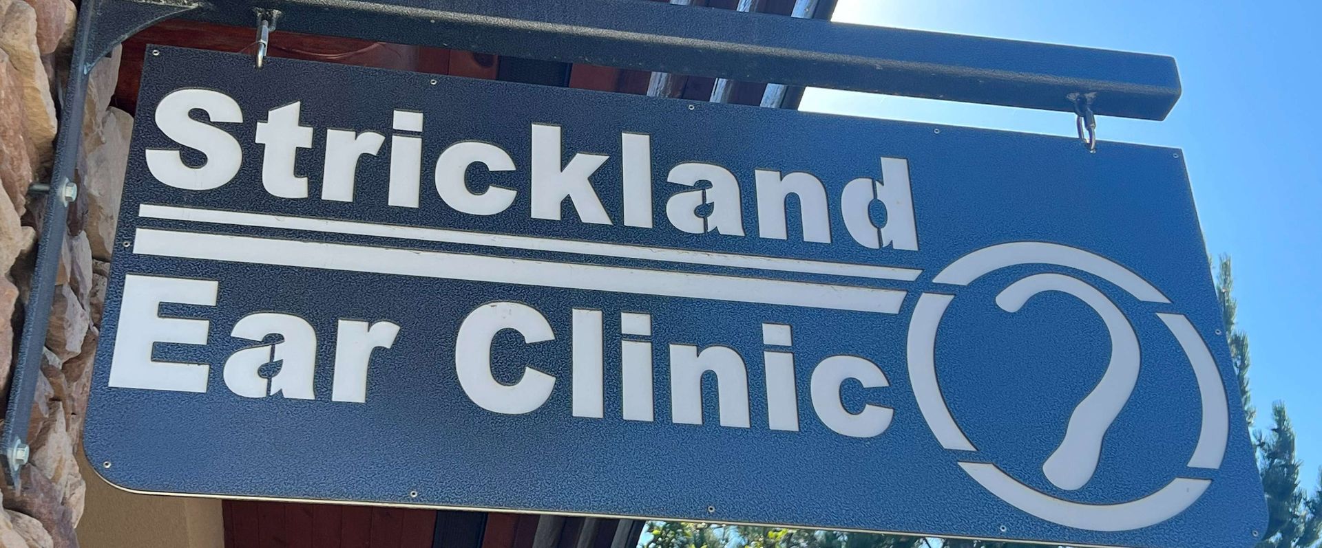 Blue sign reading “Strickland Ear Clinic” with a white ear icon outdoors.