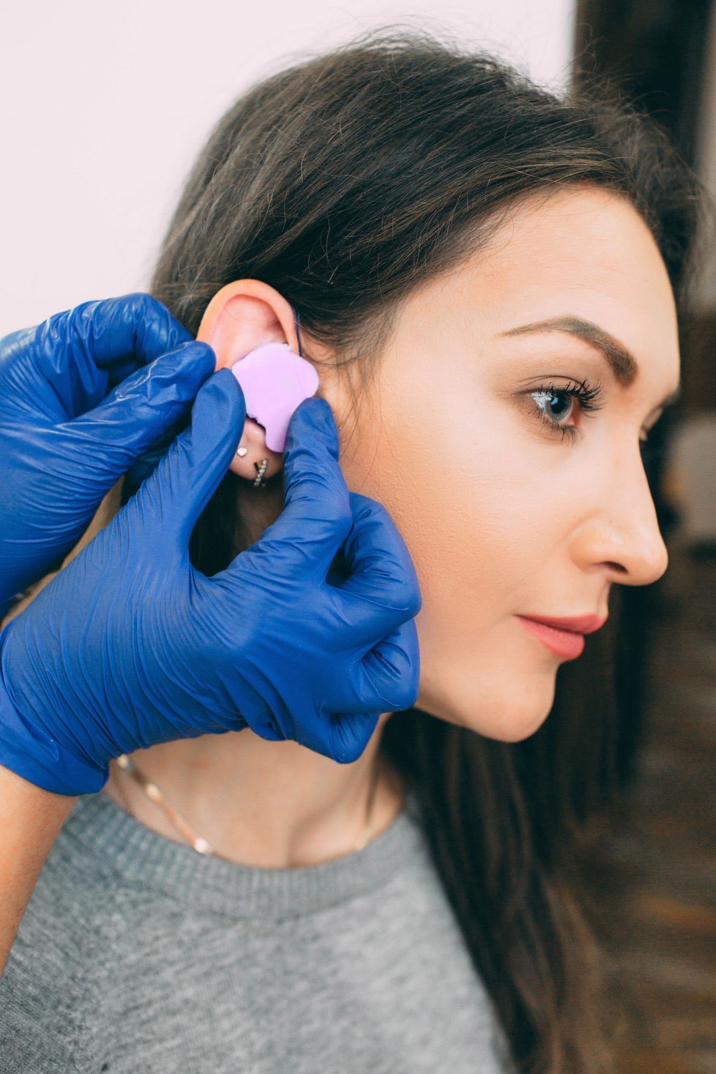 Gloved hands cleaning a woman’s ear with a pink cotton pad