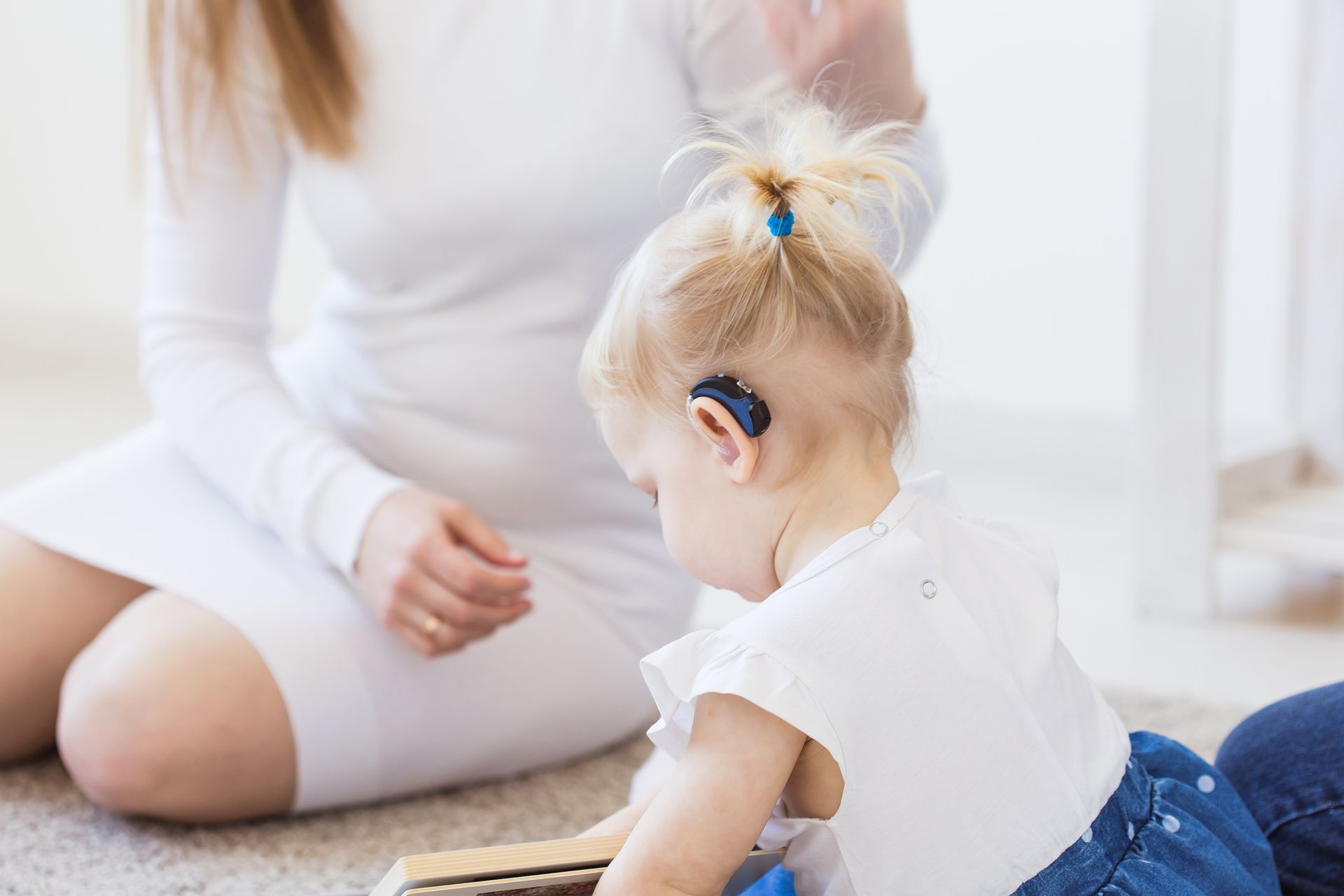 Woman and baby sitting on a bright floor, facing each other during playtime