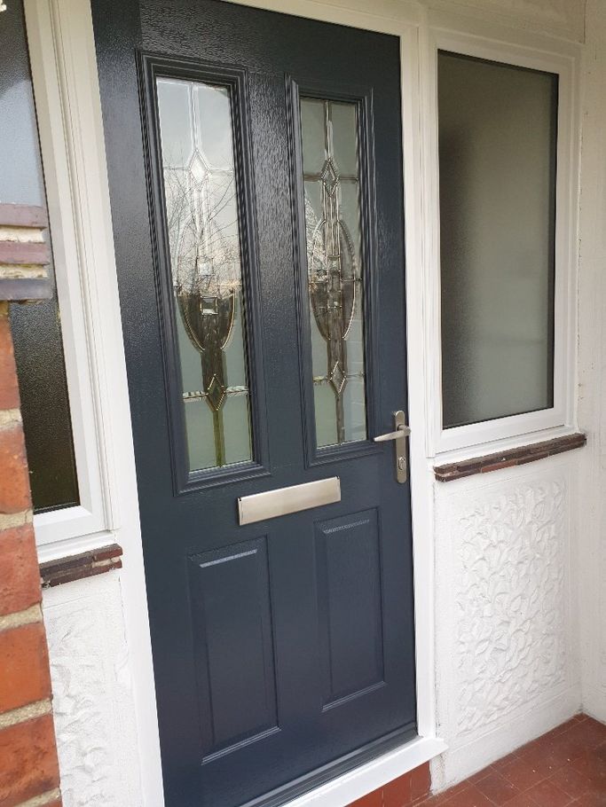 A blue door with stained glass windows is on a white brick wall.