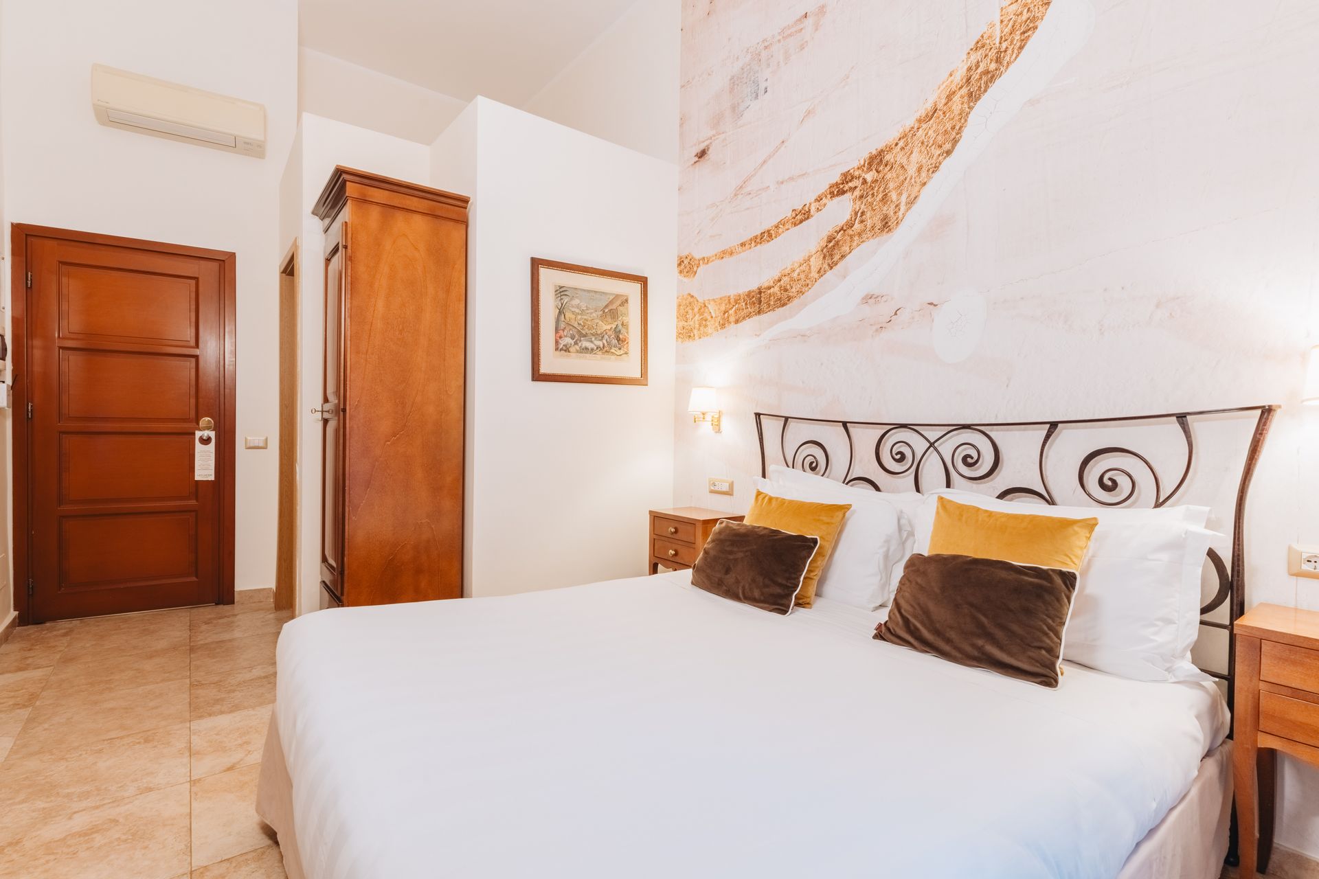 Schlafzimmer mit Bett, Nachttischen, Holztür und Kleiderschrank. Weiße Wände, goldene Akzente und Marmorboden.